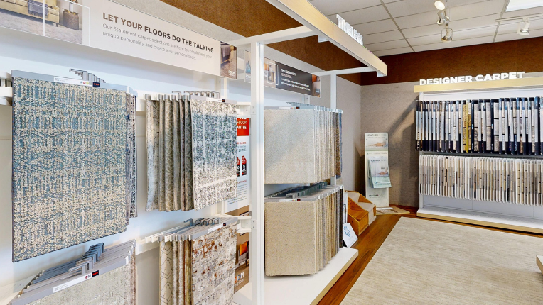 A retail showroom displaying a variety of carpet and flooring samples hanging on racks, with